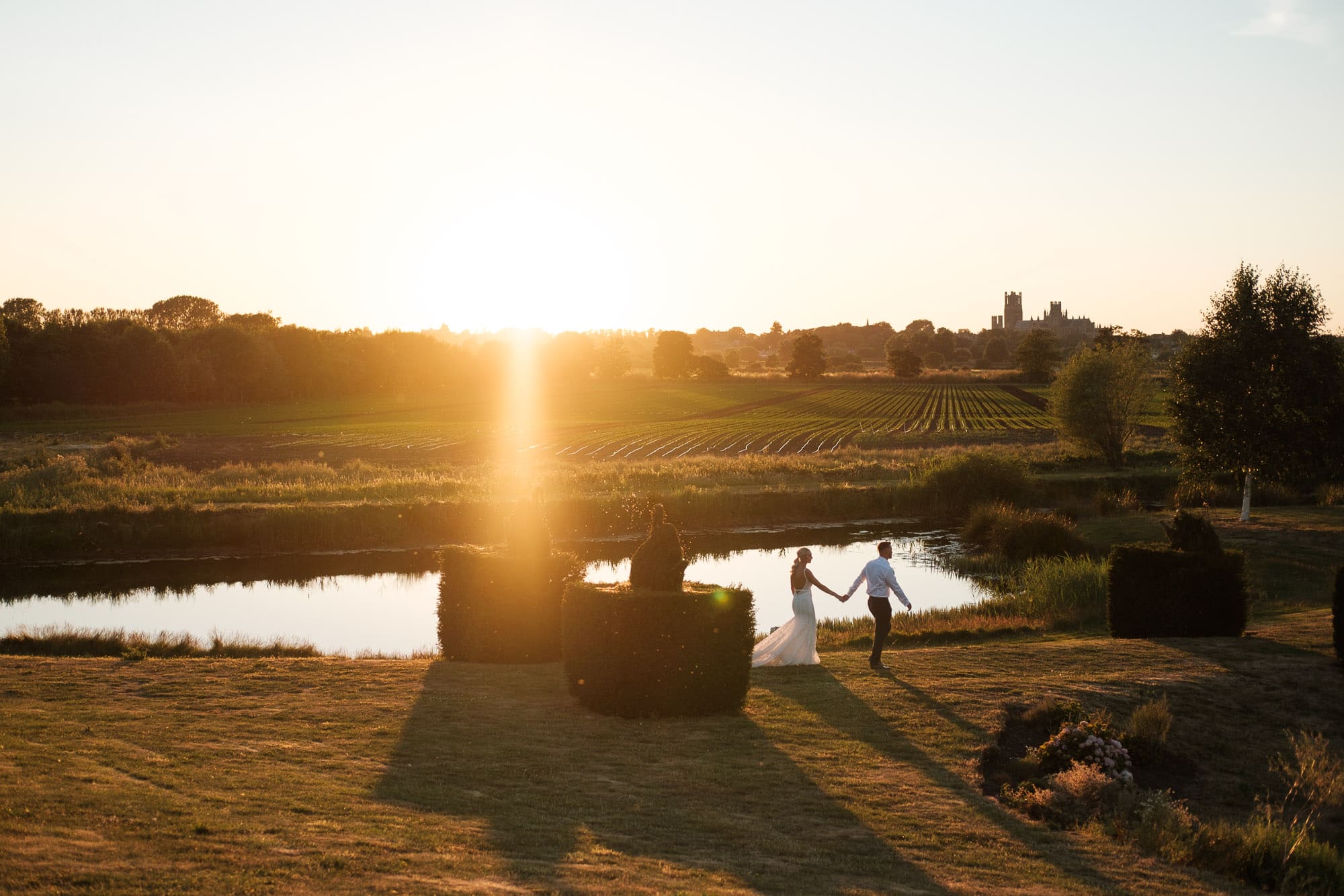 Bride and groom walking through the grounds at The Old Hall in Ely as the sun sets