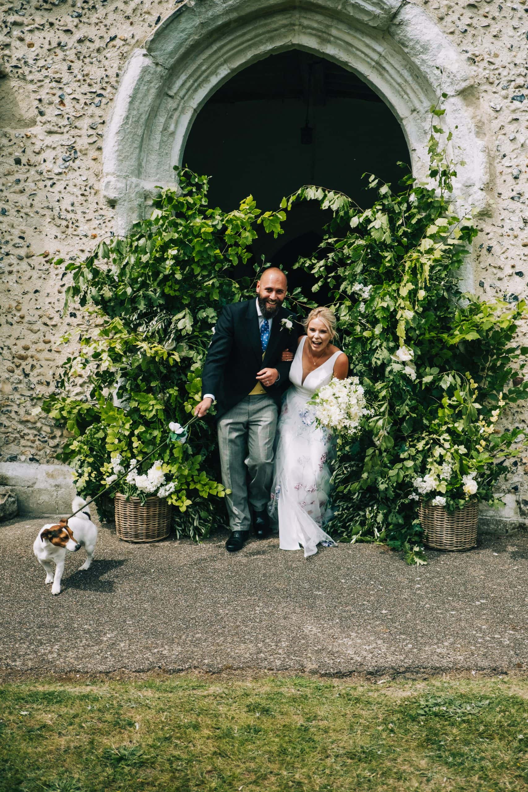 Bride and groom squeeze through the flower arch outside the church