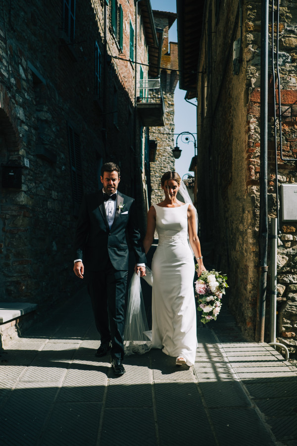 Bride and groom walking with light coming through the buildings of Bride and groom walking through the streets of Passignano