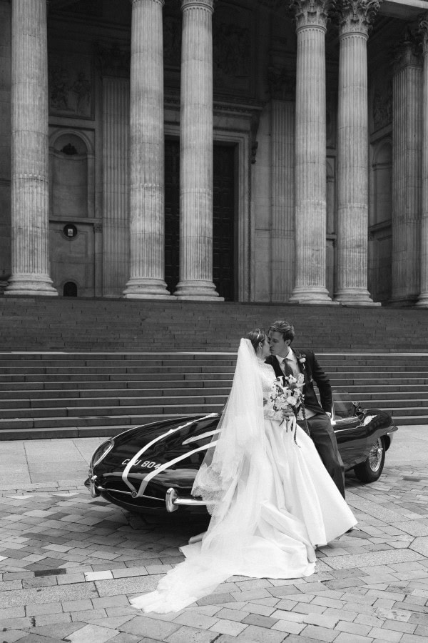 Bride and groom kiss sitting on a old style Jaguar in front of St Paul's Cathedral in London